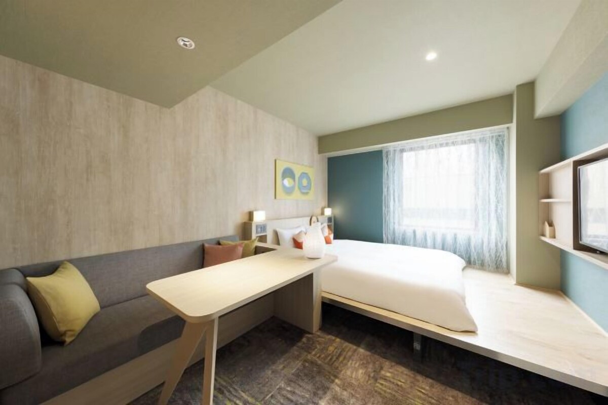 Quarto de hotel moderno com cama, sofá, mesinha e televisão.