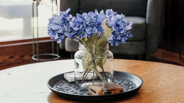 A round wooden table with a glass vase containing blue flowers and a tray with small items. - Relax & Recharge: Mid-Century Modern Home with Sauna in Spring Green (Spring Green)