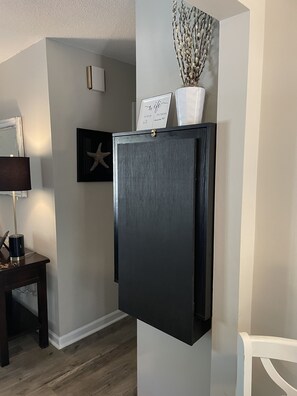 A modern kitchen with a built-in black refrigerator, a small table with a lamp, and a framed picture on the wall.