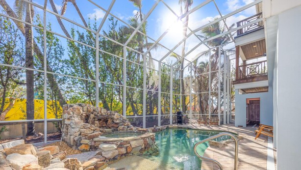 A glass-enclosed pool area with a stone waterfall, surrounded by a white structure and trees. - Ready for Rentals- All New Kitchen- Stunning Interior (Captiva)