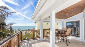 A covered outdoor area with a wooden table and chairs, a view of the ocean, and a building in the background. - Ready for Rentals- All New Kitchen- Stunning Interior (Captiva)