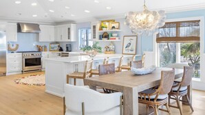 A modern kitchen with white cabinetry, a central island, and a dining area with wicker chairs. - Ready for Rentals- All New Kitchen- Stunning Interior (Captiva)