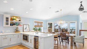 A spacious kitchen with white cabinetry, a central island, and a dining area with wooden furniture. - Ready for Rentals- All New Kitchen- Stunning Interior (Captiva)