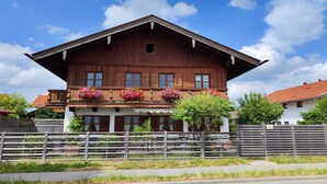 Un chalet traditionnel en bois, doté d’un balcon orné de fleurs aux couleurs vives, d’un toit à pente et d’une clôture en bois en premier plan.