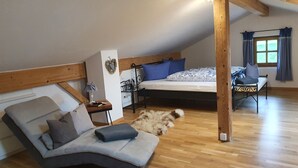 Une chambre à coucher confortable, aménagée en style «loft», avec un lit, un canapé, une petite table et une fenêtre avec des rideaux.