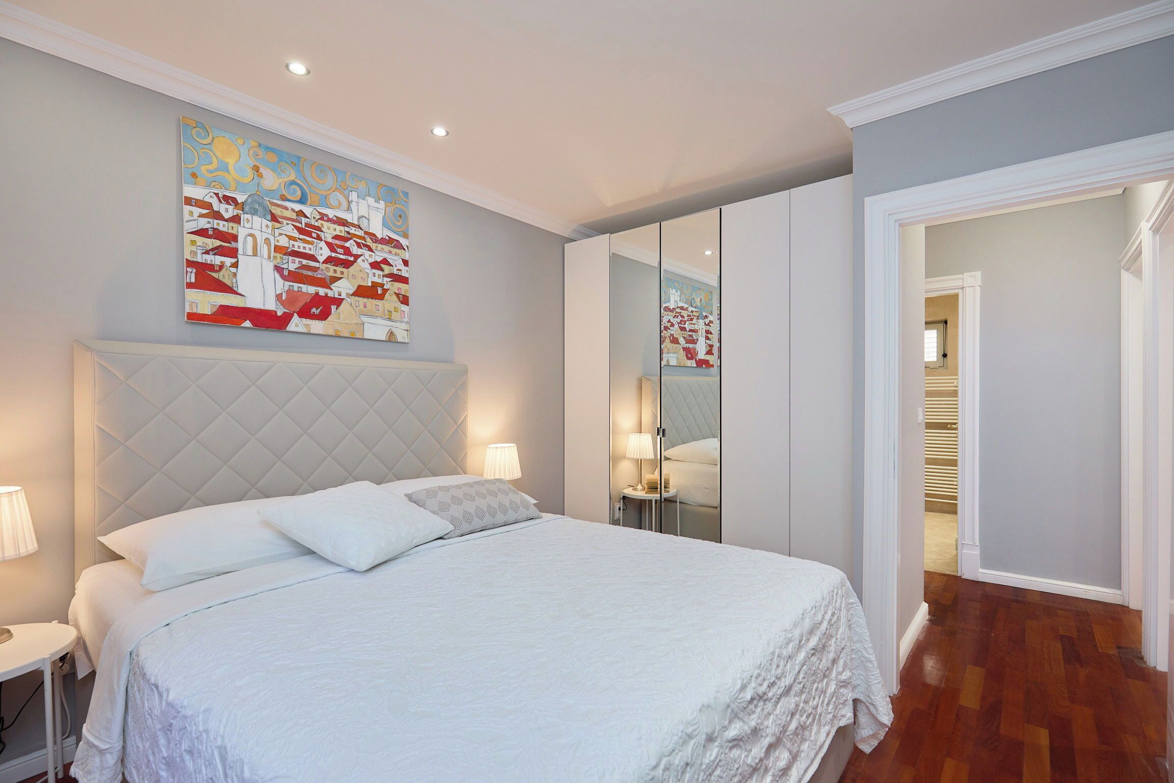 A bedroom with a large bed, a headboard, bedside tables with lamps, and a wall-mounted painting.