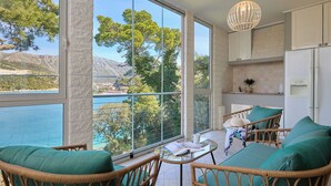 A balcony with wicker furniture, a table, and a view of a body of water and trees. - Hedera Estate, Hedera A3 (Dubrovnik)