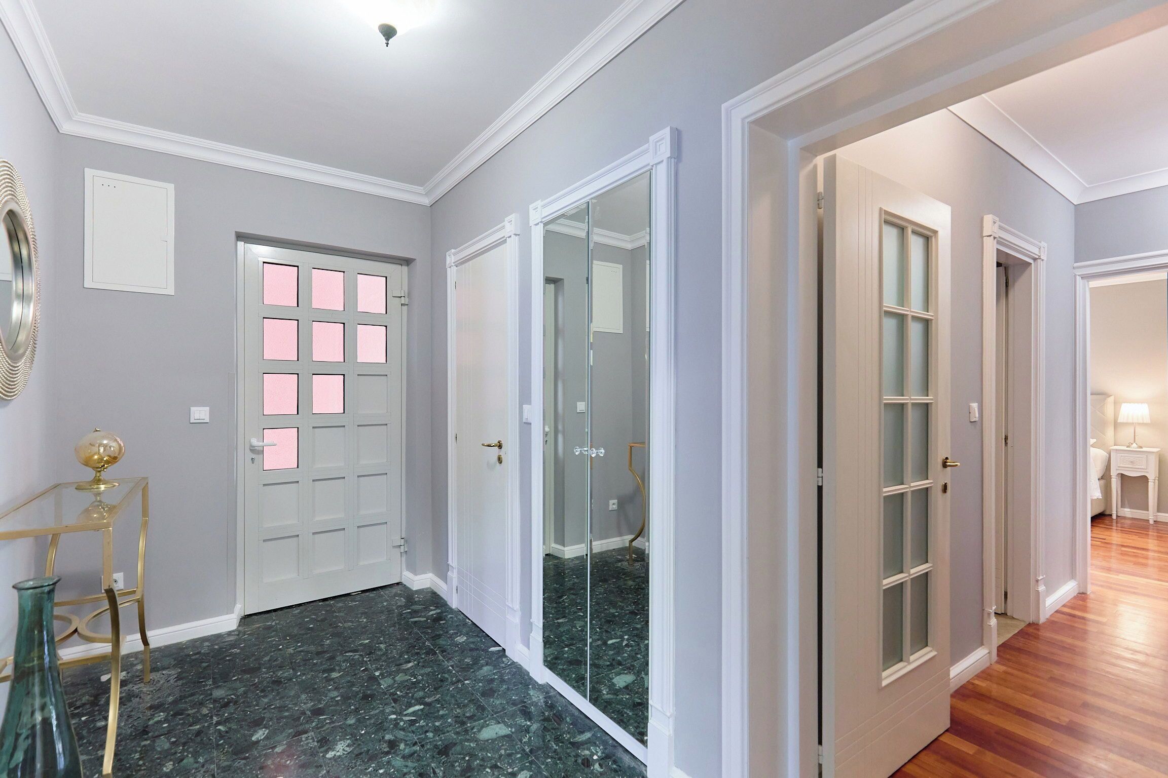 A hallway with a marble floor, white doors with glass panels, and a small table with a globe.