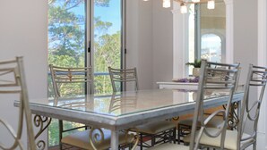 A dining area with a glass table and metal chairs, large windows with a view of trees, and a chandelier. - Hedera Estate, Hedera A3 (Dubrovnik)