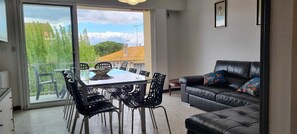 Varanda com porta de vidro, mesa de jantar com cadeiras e sofá de couro preto com almofadas coloridas.