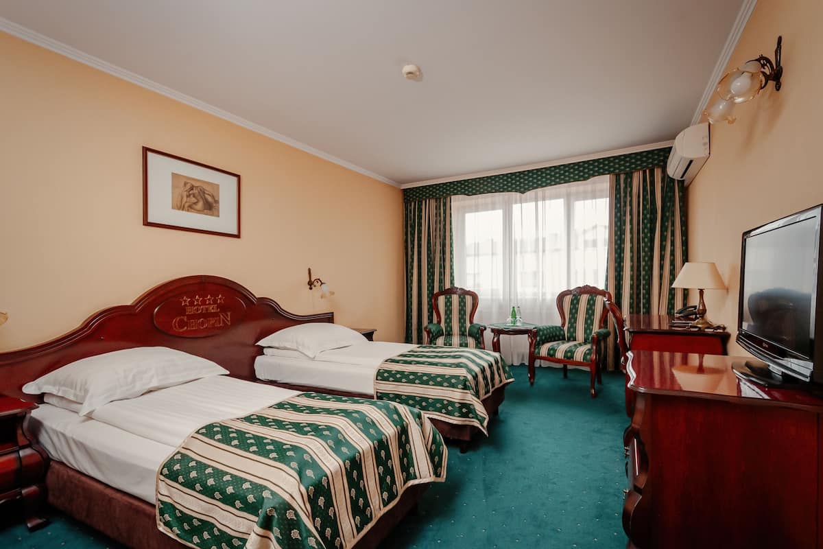 A hotel room with two beds, a television, a desk, and a chair.