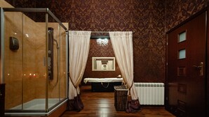 Ein Zimmer mit einer Glaskabine zur Dusche, einem Bett mit weißer Bettdecke, einer Kommode und einem Heizkörper.