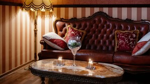 Ein Zimmer mit einer gepolsterten Ledersofa, einem runden Marmortisch mit Kerzen und einer Stehlampe.