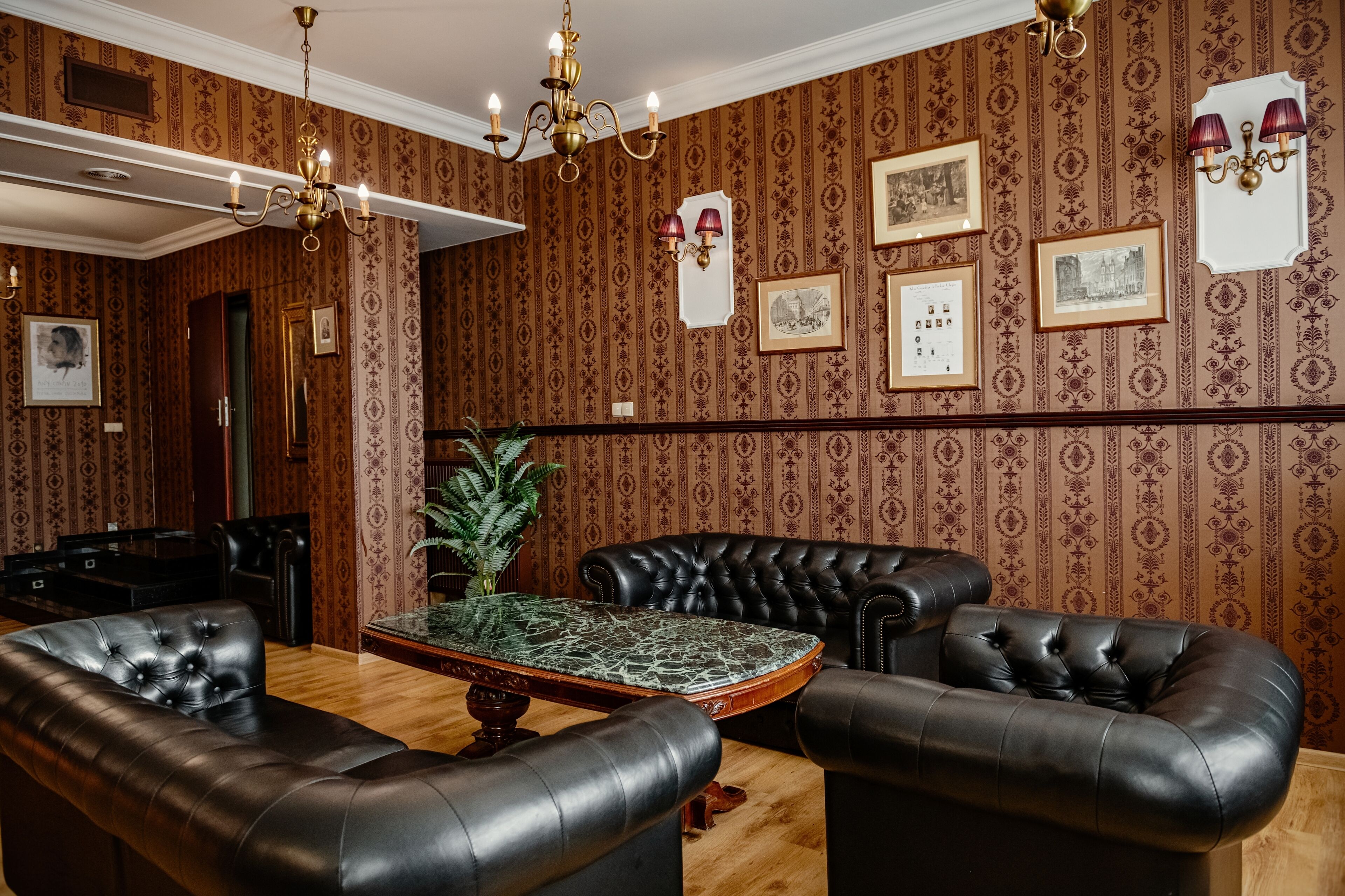 Een kamer met behang met patroon, een kroonluchter, een piano en lederen meubels.