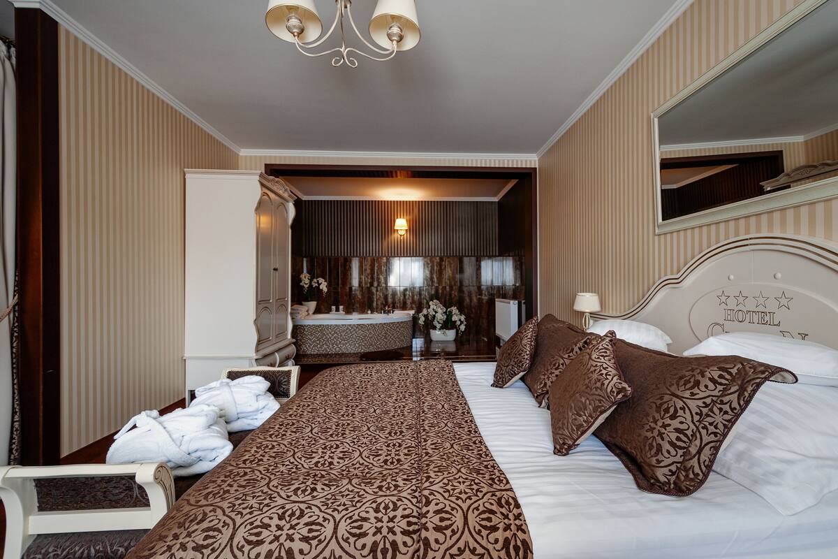 A hotel room with a large bed, a vanity with a mirror, a chandelier, and a view of the bathroom.