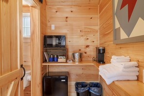Uma cabana de madeira compacta com cozinha compacta, micro-ondas, máquina de café e lixeira.