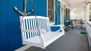 Une balançoire blanche suspendue à un mur en bois bleu, avec une fenêtre et une porte.