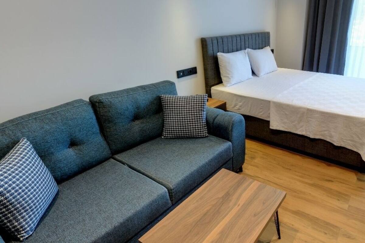 A modern hotel room with a sofa, a single bed, a wooden coffee table, and a wardrobe.
