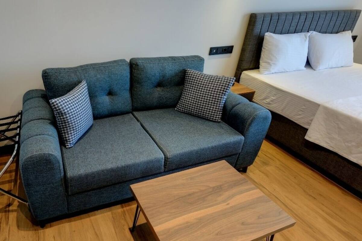 A modern room with a grey sofa, two pillows, a wooden coffee table, and a bed with white bedding.