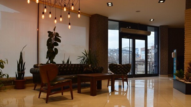 A modern lobby with a leather sofa, wooden chairs, and potted plants. - Gorukle Alpas Yasam Hotel (Bursa)