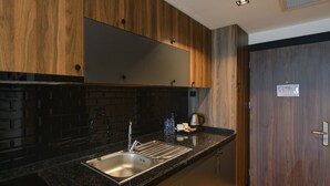 A modern kitchen with a black countertop, stainless steel sink, and wooden cabinets. - Gorukle Alpas Yasam Hotel (Bursa)