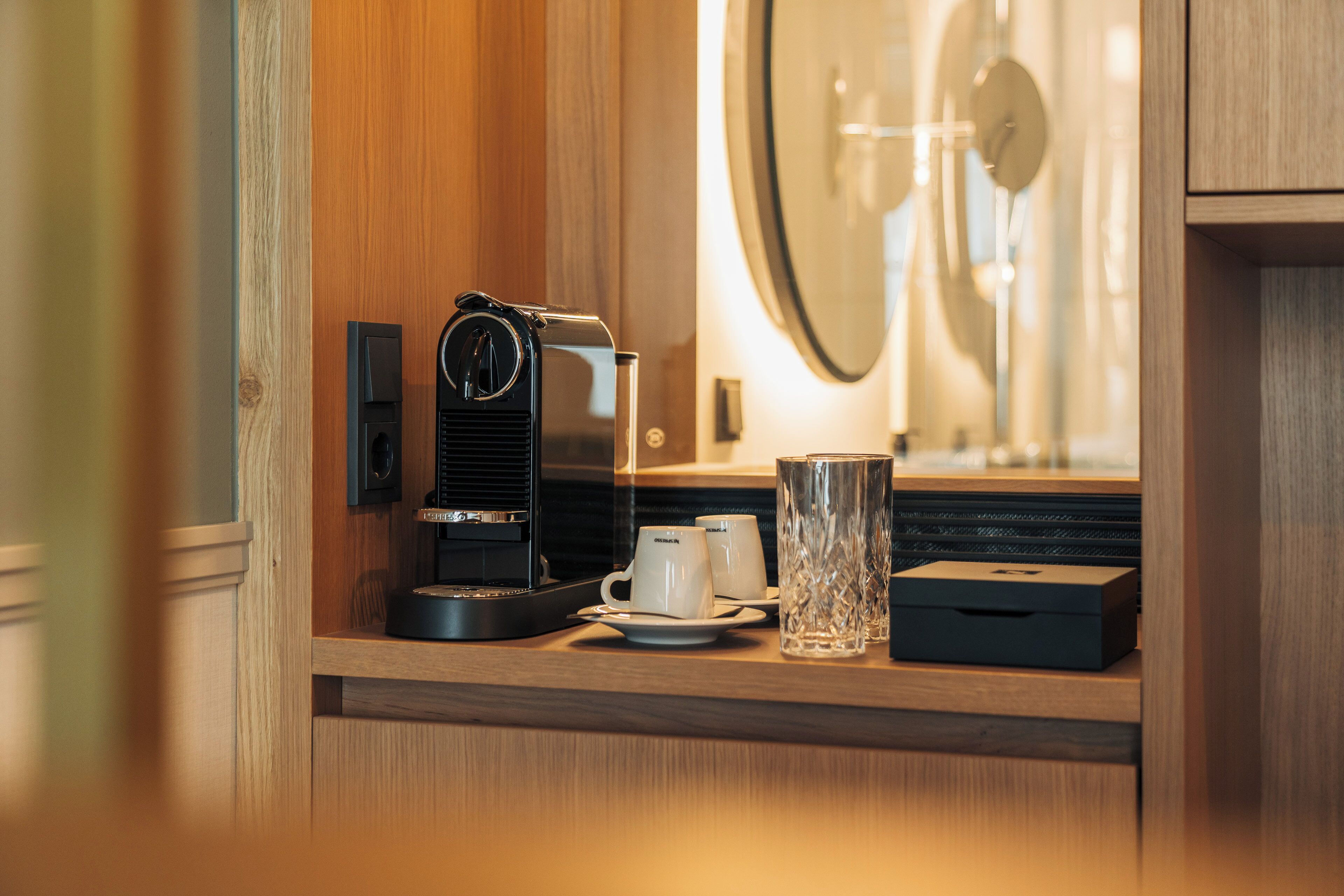 A coffee machine on a wooden counter with two white cups and a glass.