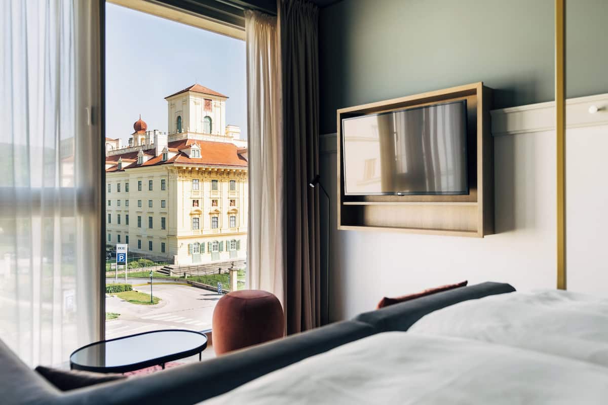 Habitación de hotel con una ventana grande, una cama, un televisor y una pequeña mesa.