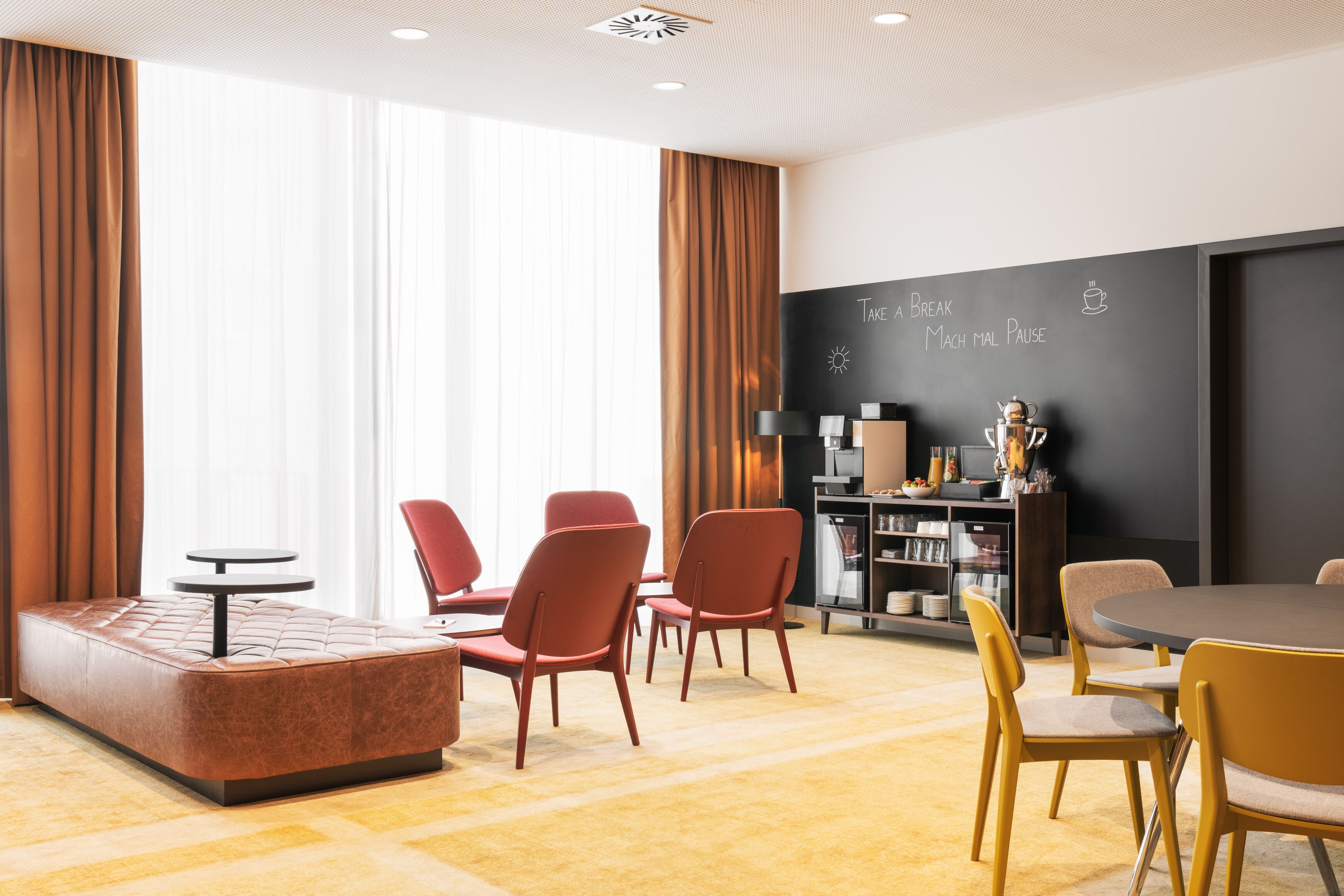 A modern lounge area with a sofa, chairs, a round table, and a chalkboard with motivational writing.