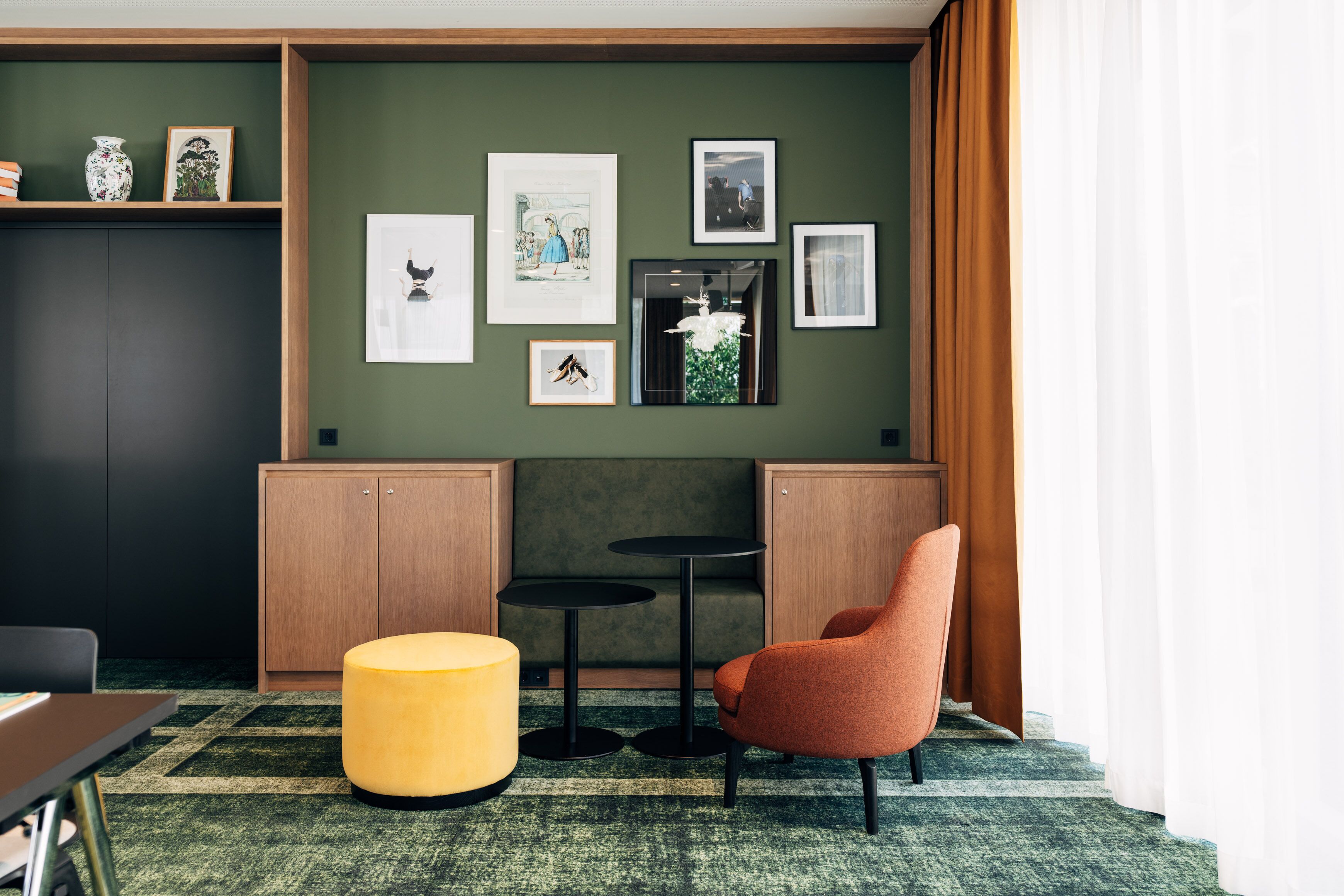 A modern room with a green wall, wooden cabinets, a round yellow ottoman, a red chair, and a black table.