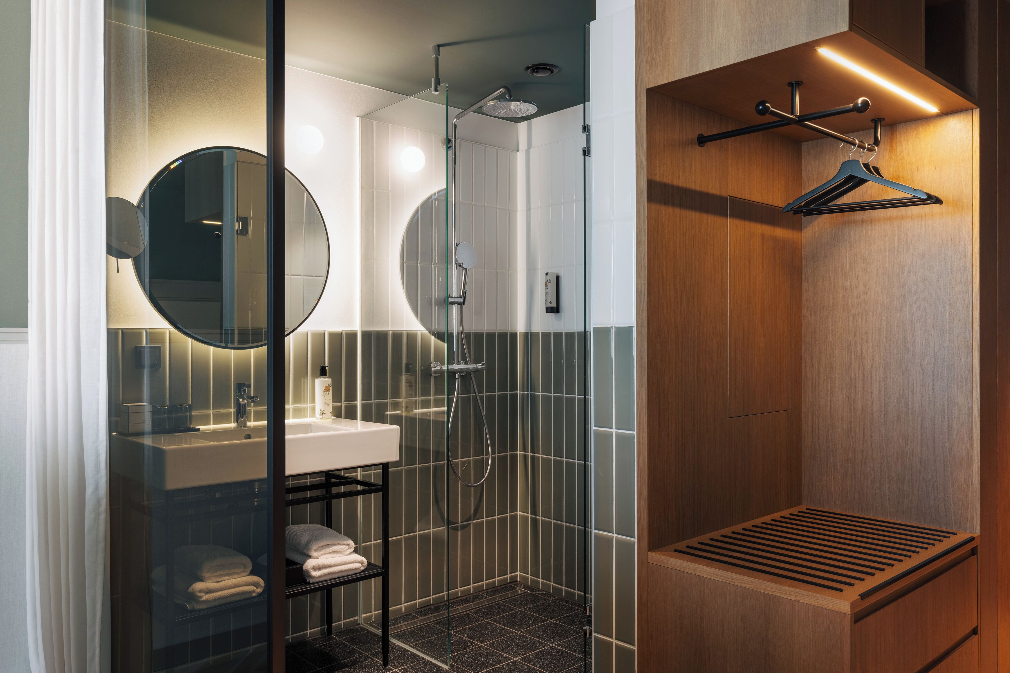 A modern bathroom with a glass-enclosed shower, a round mirror, a sink, and a wooden vanity.