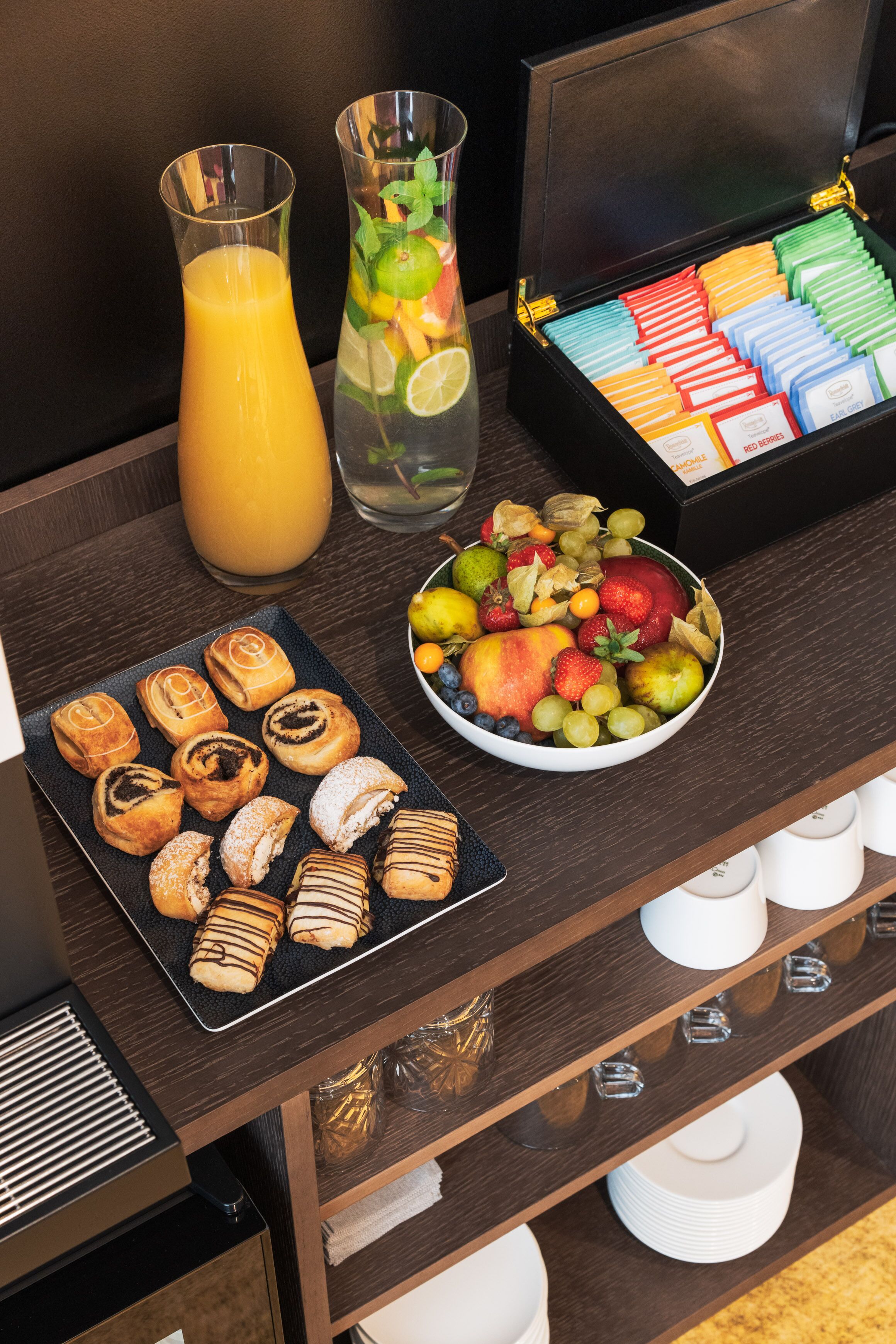 Un bufé de desayuno con bollería, frutas, zumos y bolsitas de té.