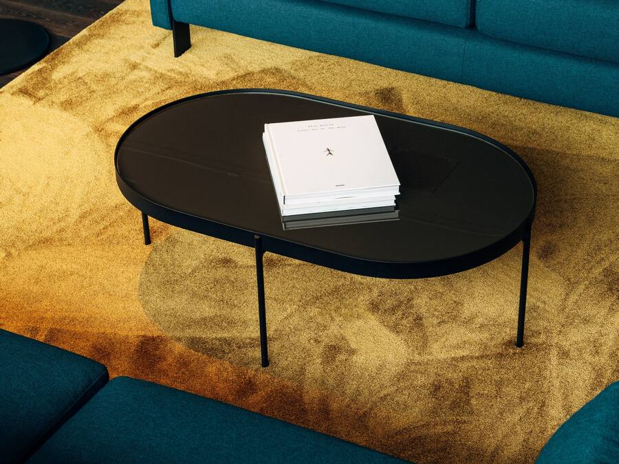 Un saló modern amb un sofà color turquesa, una taula de café negra i una catifes daurada decorativa.