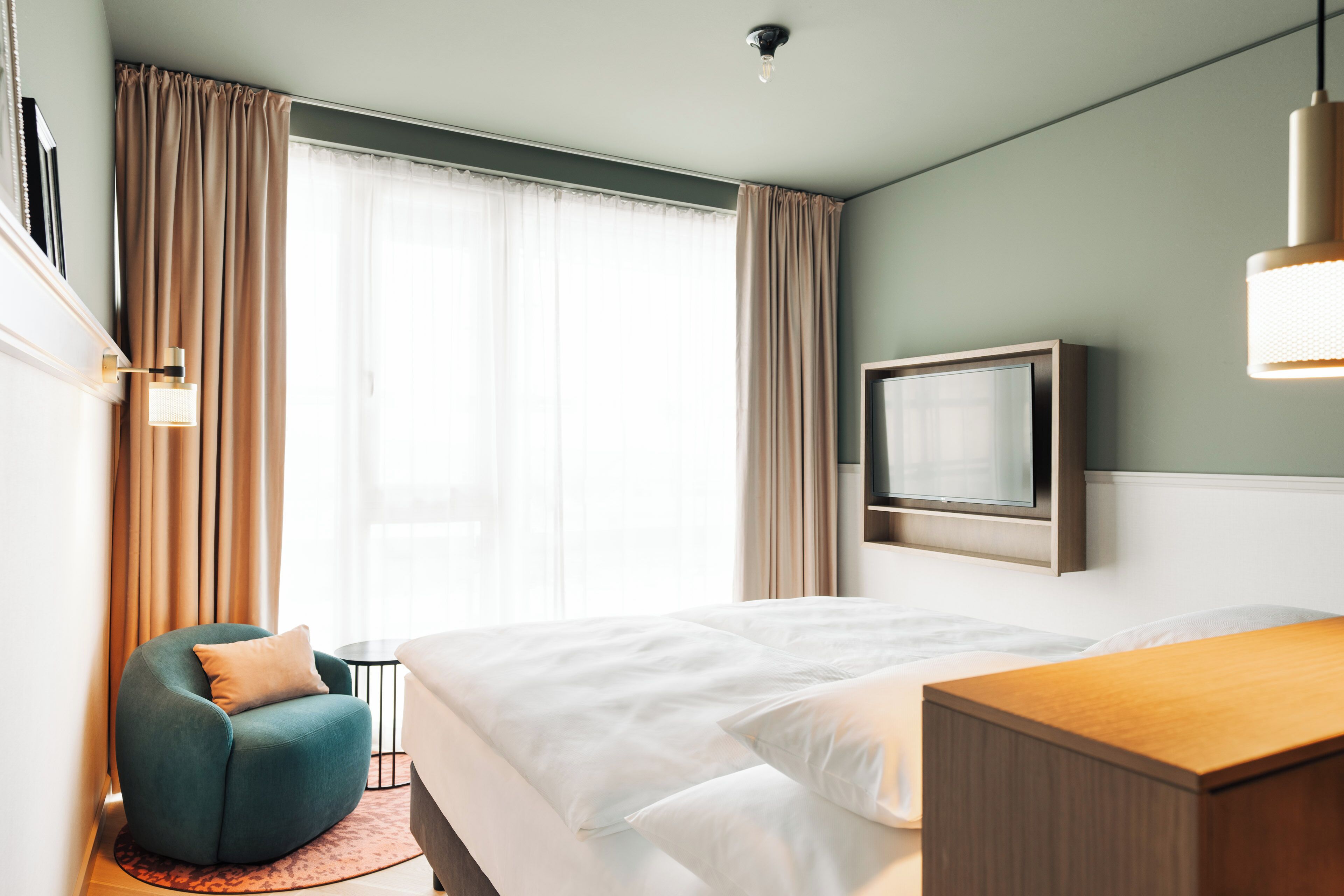 Una habitación de hotel con cama, escritorio, silla, televisor y cortinas.