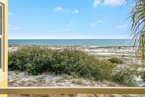Une vue depuis un balcon donnant sur une plage à la végétation clairsemée, sous un ciel dégagé.