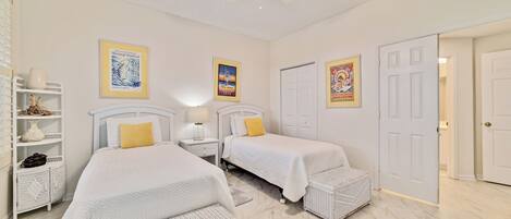 A bedroom with two beds, a ceiling fan, and a door leading to another room.