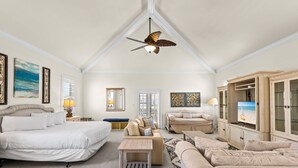 A spacious bedroom with a large bed, a sitting area with a sofa and armchair, a ceiling fan, and a TV in a cabinet. - Gated Community, Open Floor Plan, Private Screened Pool (Destin)