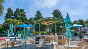 A covered outdoor seating area with tables and chairs, a children's play structure, and a sandy ground. - Gated Community, Open Floor Plan, Private Screened Pool (Destin)