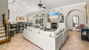 A spacious living area with a large sofa, a dining area with chairs, a kitchen with a fireplace, and a staircase. - Gated Community, Open Floor Plan, Private Screened Pool (Destin)