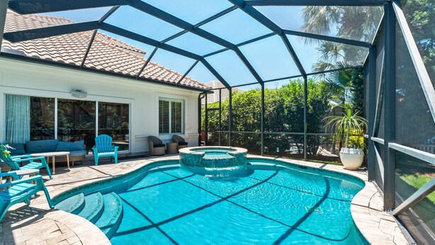 A covered swimming pool with a hot tub, outdoor seating, and a view of a house with a tiled roof. - Gated Community, Open Floor Plan, Private Screened Pool (Destin)