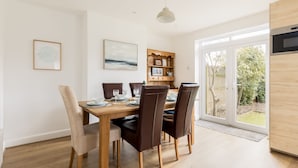 Un comedor con una mesa y sillas de madera, una lámpara colgante y vistas al exterior a través de un ventanal.