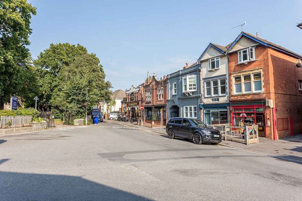 A street view with a car parked on the side, buildings with shops, and a clear sky.