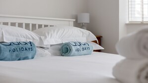 Una cama bien hecha con almohadas blancas y azules, una de las cuales tiene bordado el texto "QUAY HOLIDAYS".