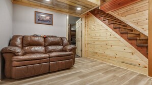 Una habitación con un sofá de cuero marrón, piso de madera, una escalera de madera y un cuadro en la pared.