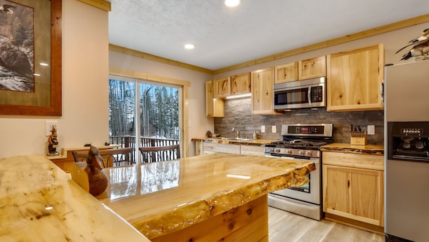 Una cocina moderna con armarios de madera, una isla grande, electrodomésticos de acero inoxidable y vistas al bosque.