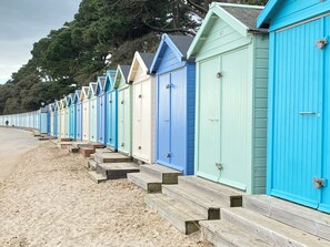 A row of colorful beach huts with wooden steps leading up to them, lined up along a sandy beach.