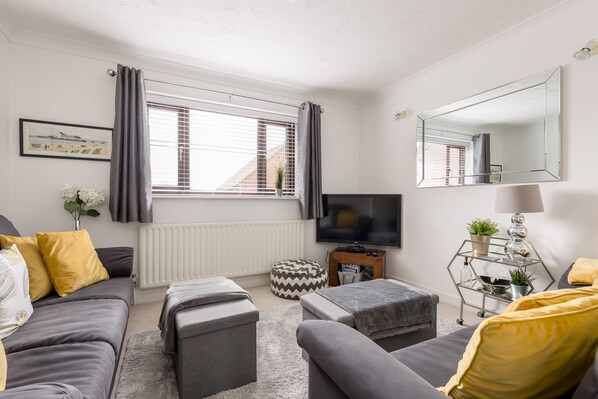 A modern living room with a grey sofa, ottomans, a TV, and a window with curtains.