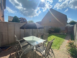 A patio with a glass table and chairs, a black umbrella, and a brick house in the background.
