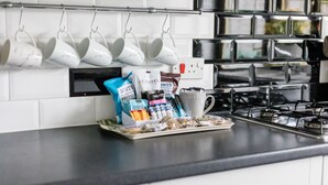 En köksbänk med vita muggar hängande på en hylla, en kaffebryggare och ett fat med kaffekapslar och en kopp.