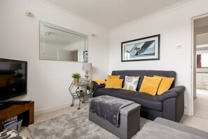 A modern living room with a grey sofa, a flat-screen TV, a large mirror, and a framed picture on the wall.