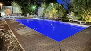 A rectangular swimming pool with a wooden deck surrounding it, set in a landscaped garden with trees and outdoor furniture. - PRETTY VILLA WITH POOL SLEEPS 8 (Tavel)